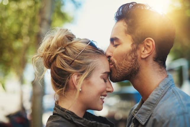 a man kissing his girlfriend’s forehead outside