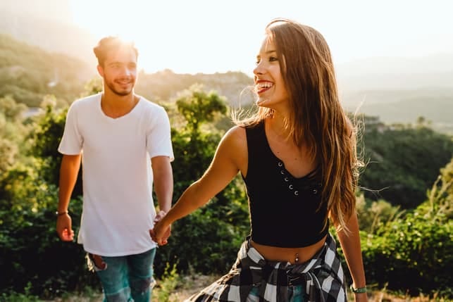 a young woman is leading her boyfriend through a park