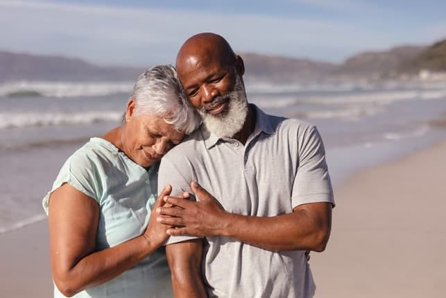 a senior couple is having a walk on a beach while cuddling