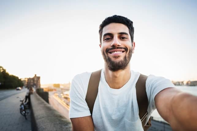 an attractive dark man talking a selfie outdoors