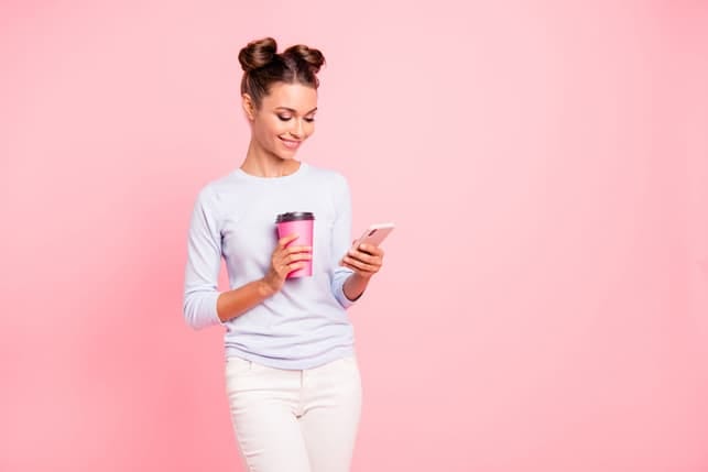 a girl is checking her phone while holding a coffee cup and smiling